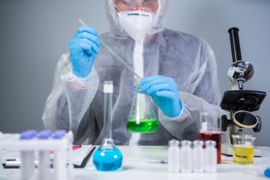 Bilim adamı yeşil sıvıyı kabın içinde sallıyor. Laboratuvarda test ya da araştırma yapan genç bir laboratuvar asistanı. Teknisyen kimya laboratuarı deneyini test ediyor ve mikroskop ile birlikte cam tüpü sallıyor..