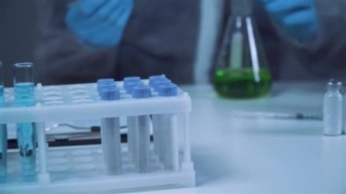 Erlenmeyer şişesinde kimya laboratuvarında yeşil sıvıyı karıştırıp sallayan koruyucu giysi teknisyeni. Laboratuvar teknisyeni kimyasal reaksiyonlar üzerinde çalışıyor ve kanser ilacı arıyor