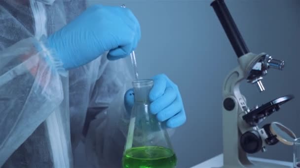 Scientist shakes green biochemical product in erlenmeyer flask mixing and research in laboratory. Lab assistant work in corona virus pandemic laboratory, COVID 19. Drug development, medical research — Stock Video