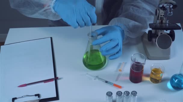 Científico agitando líquido verde en el vaso de precipitados. Asistente de laboratorio joven haciendo pruebas o investigación en laboratorio. Técnico probando experimento de laboratorio de química y agitando frasco de tubo de vidrio junto con microscopio — Vídeos de Stock