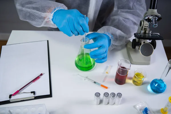 Scientist shaking green fluid in beaker. Young laboratory assistant making test or research in lab. Technician testing chemistry lab experiment and shaking glass tube flask along with microscope.