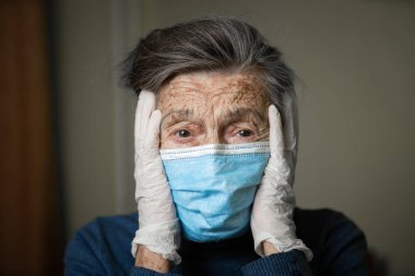Kırışıklıkları olan, tıbbi maske ve eldiven takan yaşlı beyaz bir kadının portresi. Koronavirüs salgını nedeniyle korku ve öngörülemezlik duygusu. Yaşlılar sağlık ve tıp teması.