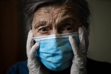 Koruyucu maskeli üzgün yaşlı kadın, koronavirüs salgını sırasında evde lateks eldivenler. Evde kal. Yaşlı nine, karantinaya alınmış salgın hastalık kovid 19 'dan emekli oldu. Maskeli kadın enfeksiyonu, bakteri gribi..