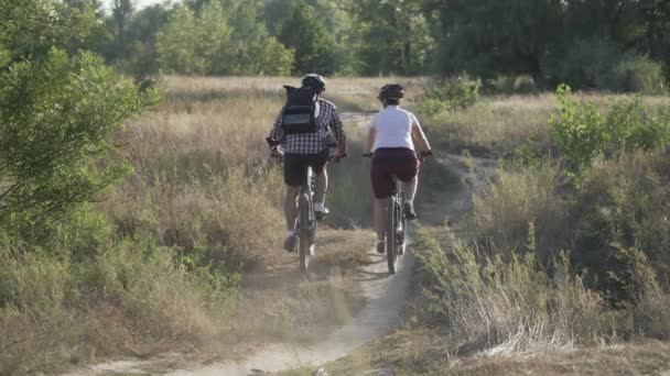 Homem e mulher andam de bicicleta de montanha juntos na estrada rural no verão natureza, tempo ensolarado. Alguns ciclistas passam o tempo ativo exercitando ao ar livre. Família esportes ciclismo fim de semana. Pessoas, estilo de vida — Vídeo de Stock