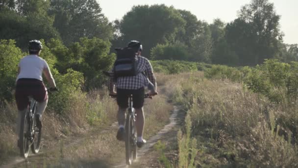 Pareja feliz en un paseo en bicicleta en el campo. Fitness, deporte, personas y concepto de estilo de vida saludable. Ciclismo de vacaciones en coutryside. Pareja activa ciclistas montar bicicletas de montaña en carretera escénica — Vídeos de Stock