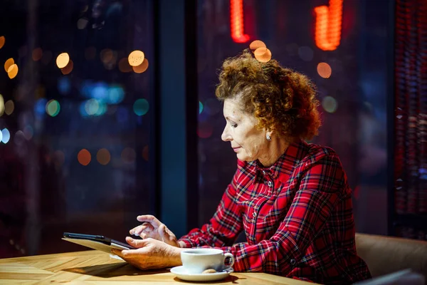 Senior woman using tablet in a cafe. Mature woman relaxing at a restaurant with tablet pc. Elderly female use digital tablet at coffee shop. Technology, old age and people concept. Mature student.
