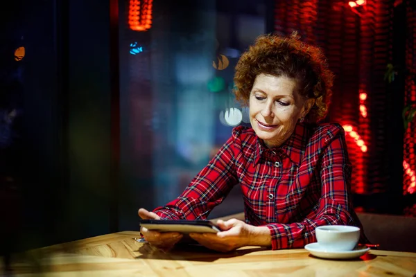 Senior woman using tablet in a cafe. Mature woman relaxing at a restaurant with tablet pc. Elderly female use digital tablet at coffee shop. Technology, old age and people concept. Mature student.