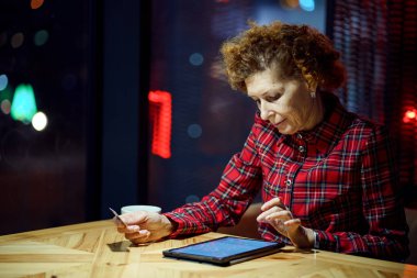 Son sınıf öğrencisi bir kadın kafede dijital tabletten Noel hediyesi sipariş ediyor. Olgun alıcının elinde tablet ve kredi kartı var. İnternetten alışveriş yapan yaşlı bir kadın. Çevrimiçi kişisel finans. Kara Cuma.