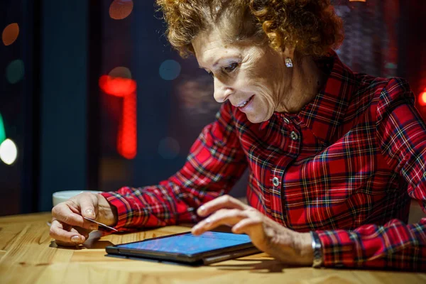 老年妇女在咖啡店的数字平板电脑上在线订购圣诞礼物 成熟的买方持有平板电脑和信用卡 老年妇女在网上购物 在线个人理财 黑色星期五 — 图库照片