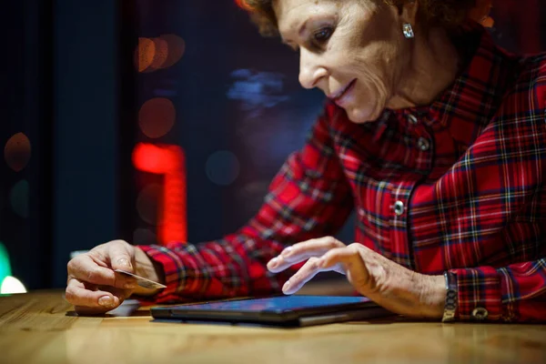 老年妇女在咖啡店的数字平板电脑上在线订购圣诞礼物 成熟的买方持有平板电脑和信用卡 老年妇女在网上购物 在线个人理财 黑色星期五 — 图库照片