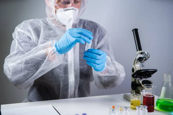 Scientist holding ampule with white powder, illegal pharmacy production, drugs. Laboratory assistant examines glass medical ampoule for injection. Penicillin dry powder medicine. Antibiotic injection.