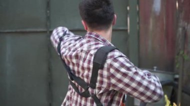 Bahçıvan kırsal evin bahçesinde çim biçme makinesiyle çalışıyor. Çiftlikte elektrikli tırpanla yabani otları kesen erkek çiftçi. Genç erkek işçi çim biçme makinesi kullanarak çim biçiyor. Benzin fırçası kesici.
