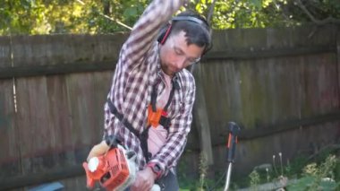 Elektrikli çim biçme makinesi ve çim biçme makinesi olan bir adam. Bahçıvan bahçe buduyor. Banliyö, köy. Beyaz tenli erkek bahçıvan avluda benzin makası ile dikiliyor. Tarlada yabani otları kesen fırça kesiciler