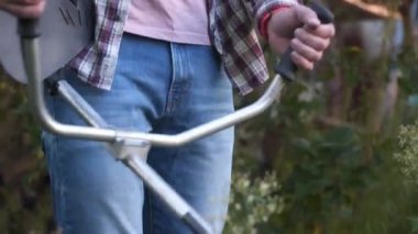 Elektrikli çim biçme makinesi ve çim biçme makinesi olan bir adam. Bahçıvan bahçe buduyor. Banliyö, köy. Beyaz tenli erkek bahçıvan avluda benzin makası ile dikiliyor. Tarlada yabani otları kesen fırça kesiciler