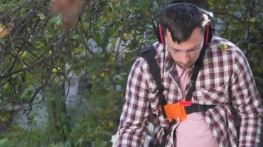 Elektrikli çim biçme makinesi ve çim biçme makinesi olan bir adam. Bahçıvan bahçe buduyor. Banliyö, köy. Beyaz tenli erkek bahçıvan avluda benzin makası ile dikiliyor. Tarlada yabani otları kesen fırça kesiciler