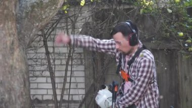 Bahçıvan kırsal evin bahçesinde çim biçme makinesiyle çalışıyor. Çiftlikte elektrikli tırpanla yabani otları kesen erkek çiftçi. Genç erkek işçi çim biçme makinesi kullanarak çim biçiyor. Benzin fırçası kesici.