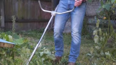 Bahçıvan kırsal evin bahçesinde çim biçme makinesiyle çalışıyor. Çiftlikte elektrikli tırpanla yabani otları kesen erkek çiftçi. Genç erkek işçi çim biçme makinesi kullanarak çim biçiyor. Benzin fırçası kesici.