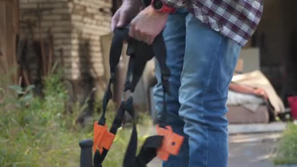 Jardinero siega hierba por cortadora de pinceles en el jardín. Hombre cortando hierba usando cortador de cepillo de gasolina. Proceso de corte de hierba con trimmer de gasolina. Trabajo de siega. Cortador, concepto de jardinería. Cortacéspedes, gente — Vídeo de stock