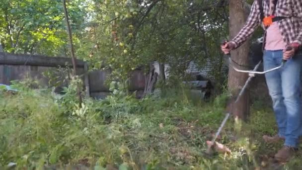 Jardinero siega hierba por cortadora de pinceles en el jardín. Hombre cortando hierba usando cortador de cepillo de gasolina. Proceso de corte de hierba con trimmer de gasolina. Trabajo de siega. Cortador, concepto de jardinería. Cortacéspedes, gente — Vídeo de stock