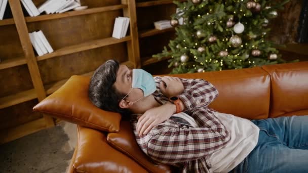 Seul la veille du Nouvel An. Concept de solitude. Solitude, dépression nerveuse Vacances de Noël pendant le confinement, quarantaine due à l'épidémie de coronavirus. Homme bouleversé dans la maison décorée à Noël en masque — Video