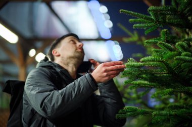 Şenlikli alışveriş, seçim ve Yeni Yıl nitelikleri satın alma. Beyaz adam telefonda konuşuyor ve yılbaşı arifesinde Noel ağacını seçmeyi tavsiye ediyor. Erkek ladin satın alır ve akıllı telefon kullanır..