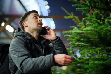 Kafkasyalı genç bir adam akşam açık hava pazarından Noel ağacını seçiyor karısıyla telefonda konuşuyor ve doğru seçim konusunda danışmanlık yapıyor. Noel ve yeni yıl tatillerinin sembolü. Tatil alışverişi..