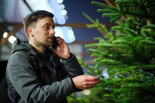 Kafkasyalı genç bir adam akşam açık hava pazarından Noel ağacını seçiyor karısıyla telefonda konuşuyor ve doğru seçim konusunda danışmanlık yapıyor. Noel ve yeni yıl tatillerinin sembolü. Tatil alışverişi..