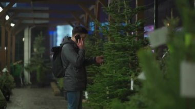 Kafkasyalı genç bir adam akşam açık hava pazarından Noel ağacını seçiyor karısıyla telefonda konuşuyor ve doğru seçim konusunda danışmanlık yapıyor. Noel ve yeni yıl tatillerinin sembolü. Tatil alışverişi.