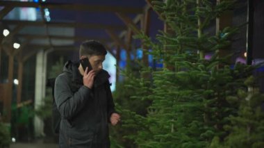 Şenlikli alışveriş, seçim ve Yeni Yıl nitelikleri satın alma. Beyaz adam telefonda konuşuyor ve yılbaşı arifesinde Noel ağacını seçmeyi tavsiye ediyor. Erkek ladin satın alır ve akıllı telefon kullanır.