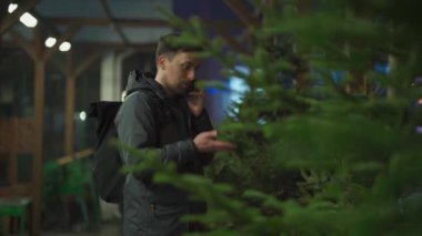 Şenlikli alışveriş, seçim ve Yeni Yıl nitelikleri satın alma. Beyaz adam telefonda konuşuyor ve yılbaşı arifesinde Noel ağacını seçmeyi tavsiye ediyor. Erkek ladin satın alır ve akıllı telefon kullanır.