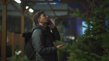 Kafkasyalı genç bir adam akşam açık hava pazarından Noel ağacını seçiyor karısıyla telefonda konuşuyor ve doğru seçim konusunda danışmanlık yapıyor. Noel ve yeni yıl tatillerinin sembolü. Tatil alışverişi.
