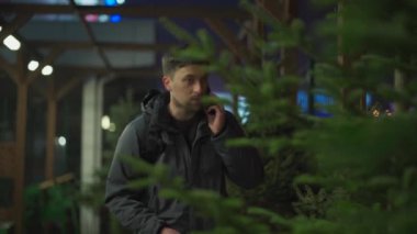 Şenlikli alışveriş, seçim ve Yeni Yıl nitelikleri satın alma. Beyaz adam telefonda konuşuyor ve yılbaşı arifesinde Noel ağacını seçmeyi tavsiye ediyor. Erkek ladin satın alır ve akıllı telefon kullanır.