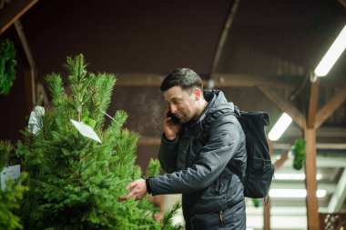 Şenlikli alışveriş, seçim ve Yeni Yıl nitelikleri satın alma. Beyaz adam telefonda konuşuyor ve yılbaşı arifesinde Noel ağacını seçmeyi tavsiye ediyor. Erkek ladin satın alır ve akıllı telefon kullanır..