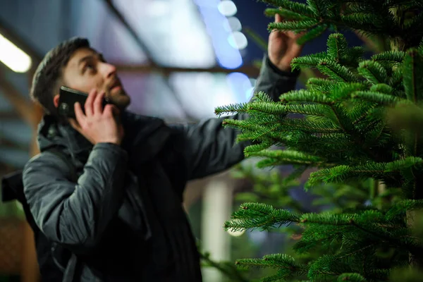 父はクリスマスツリーを買い 電話で話す 市場での木材の購入 バザーだ クリスマスセール トウヒの選択に満足しています クリスマスの買い物とお祝いの準備 — ストック写真