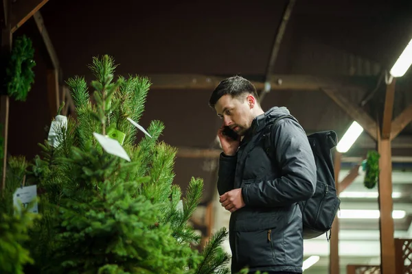 Şenlikli alışveriş, seçim ve Yeni Yıl nitelikleri satın alma. Beyaz adam telefonda konuşuyor ve yılbaşı arifesinde Noel ağacını seçmeyi tavsiye ediyor. Erkek ladin satın alır ve akıllı telefon kullanır..