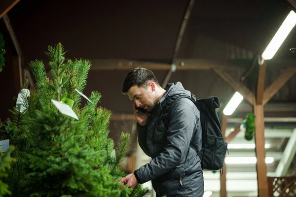 Şenlikli alışveriş, seçim ve Yeni Yıl nitelikleri satın alma. Beyaz adam telefonda konuşuyor ve yılbaşı arifesinde Noel ağacını seçmeyi tavsiye ediyor. Erkek ladin satın alır ve akıllı telefon kullanır..