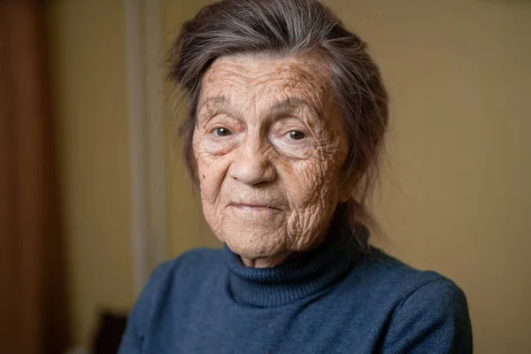 Elderly Caucasian senior grandmother ninety years old looks attentively and smiles, feels happy, large portrait, face with deep wrinkles, gray hair. Theme pensioners, old people and long-lived woman.