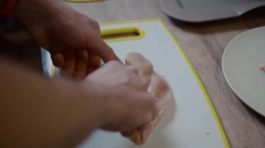 Elleri plastik panoda tavuk filetosu dilimliyor. Erkek, mutfakta tavuk keser. İşlem et yapıyor, eller kapalı. Ev yemeği konsepti. Fileto ve çiğ et. Bekar adam yemek hazırlıyor.