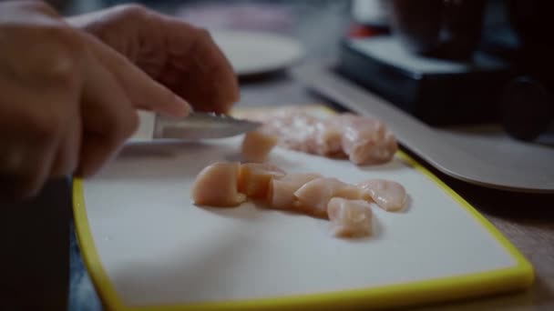 Mutfakta tavuk göğsünü bıçakla pişirme işlemi. Genç koca karısına mutfakta yardım ediyor, beyaz plastik bir tahtada taze tavuk göğsü eti kesiyor. Sağlıklı yemekler, beslenme kanatları. — Stok video