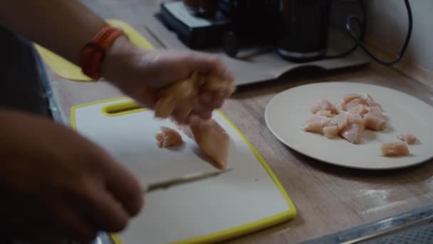 Process för matlagning kyckling bröst i kök med kniv. Ung make hjälper sin fru i köket, skär färsk kyckling bröst kött på en vit plasttavla. Matlagning av hälsosam mat, fjäderfä — Stockvideo