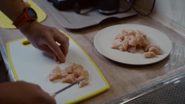 Окремі руки кавказького молодого самця ріжуть свіже куряче м'ясо на пластиковій білій дошці вдома на кухні. Хобі готує, холостяк готує вечерю. Одинокий чоловік готує птицю до обіду. — стокове відео