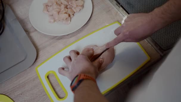 プラスチック板の上でチキンフィレをスライス男の手。男性は台所で鶏肉を切る。肉を作るプロセス,手を閉じる.家庭料理のコンセプト。フィレと生肉をカットします。学士夕食の準備家 — ストック動画