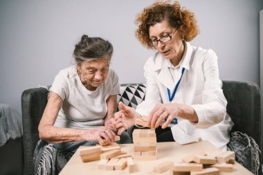 Bunama terapisi, parmaklar ve motor beceriler geliştirmek, kuleye tahta bloklar yapmak, Jenga oynamak. Yaşlı kadın 90 yaşında ve doktor huzurevinde eğitim oyunu oynuyor.