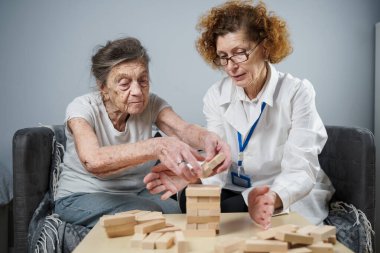 Bunama terapisi, parmaklar ve motor beceriler geliştirmek, kuleye tahta bloklar yapmak, Jenga oynamak. Yaşlı kadın 90 yaşında ve doktor huzurevinde eğitim oyunu oynuyor.