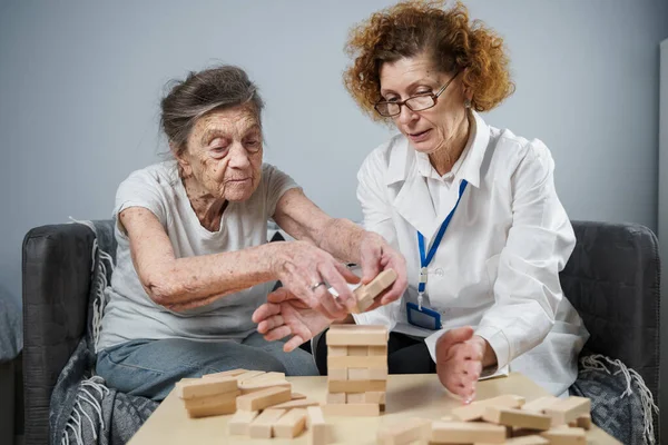 Bunama terapisi, parmaklar ve motor beceriler geliştirmek, kuleye tahta bloklar yapmak, Jenga oynamak. Yaşlı kadın 90 yaşında ve doktor huzurevinde eğitim oyunu oynuyor.