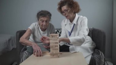 Bunama terapisi, parmaklar ve motor beceriler geliştirmek, kuleye tahta bloklar yapmak, Jenga oynamak. Yaşlı kadın 90 yaşında ve doktor huzurevinde eğitim oyunu oynuyor