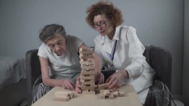 Bunama terapisi, parmaklar ve motor beceriler geliştirmek, kuleye tahta bloklar yapmak, Jenga oynamak. Yaşlı kadın 90 yaşında ve doktor huzurevinde eğitim oyunu oynuyor