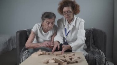 Jenga oynayan yaşlı kadın, bloklardan kule inşa ediyor. Beyaz laboratuvar önlüklü yaşlı doktor, kıdemli hastayı destekliyor, mantık geliştiriyor, iyi motor beceriler geliştiriyor, evde yaşlı yalnız kadın hastalıkları var.