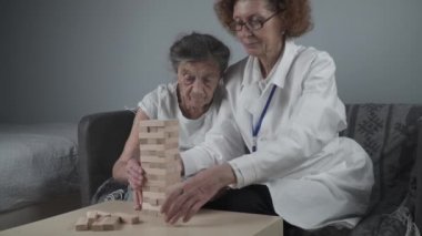 Jenga oynayan yaşlı kadın, bloklardan kule inşa ediyor. Beyaz laboratuvar önlüklü yaşlı doktor, kıdemli hastayı destekliyor, mantık geliştiriyor, iyi motor beceriler geliştiriyor, evde yaşlı yalnız kadın hastalıkları var.
