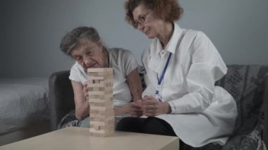 Bunama terapisi, parmaklar ve motor beceriler geliştirmek, kuleye tahta bloklar yapmak, Jenga oynamak. Yaşlı kadın 90 yaşında ve doktor huzurevinde eğitim oyunu oynuyor